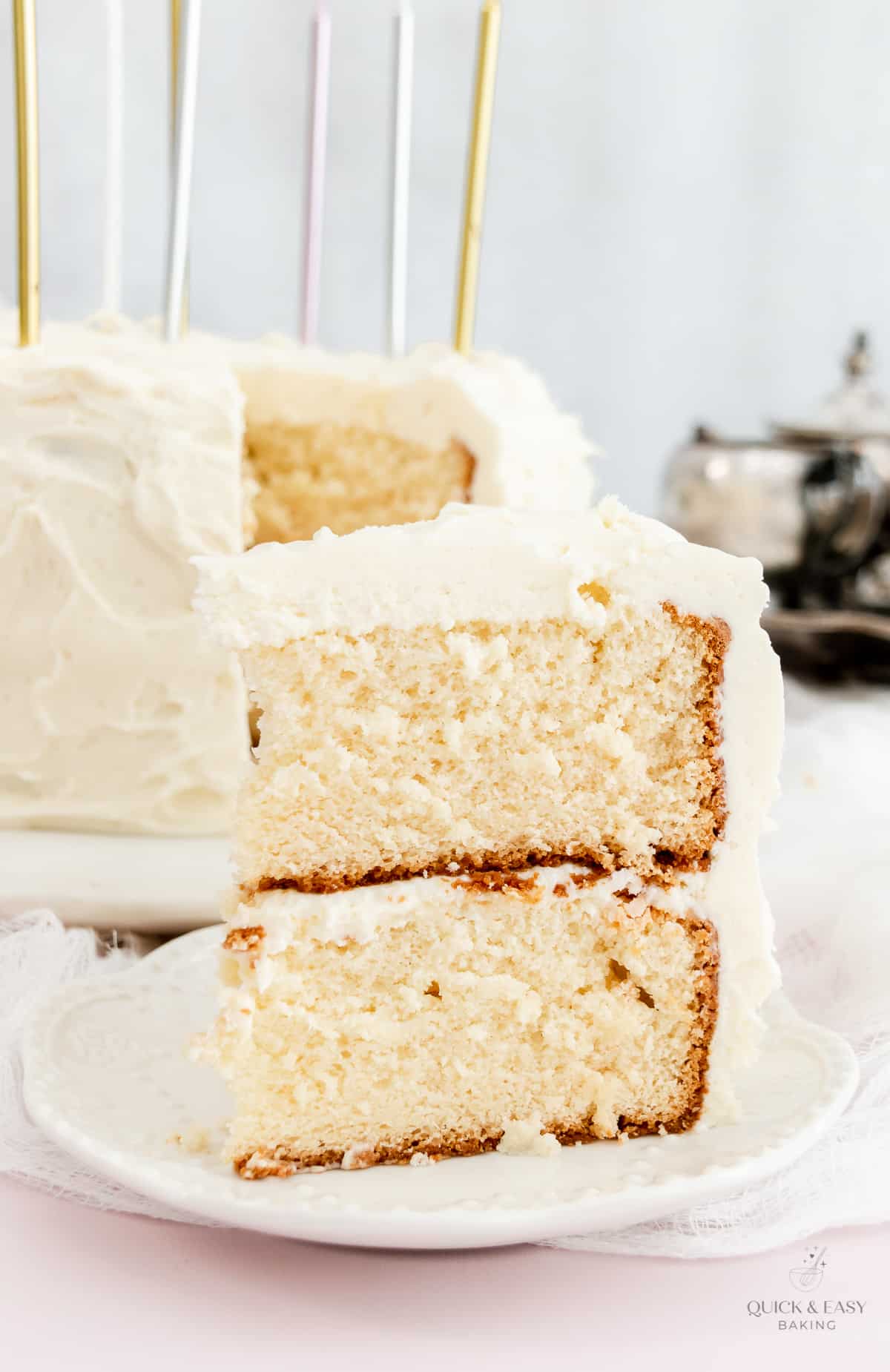 Standing slice of white cake with white chocolate frosting on a plate.