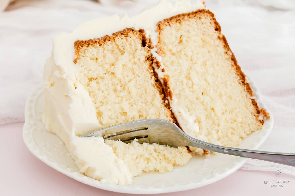 Large slice of white chocolate cake with a fork on a plate.
