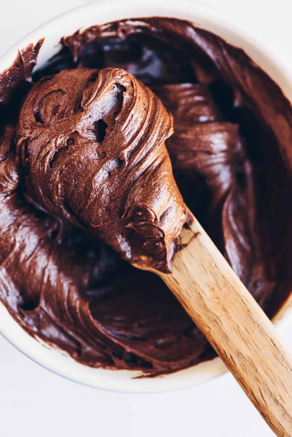 Chocolate buttercream in a bowl with wooden spoon.