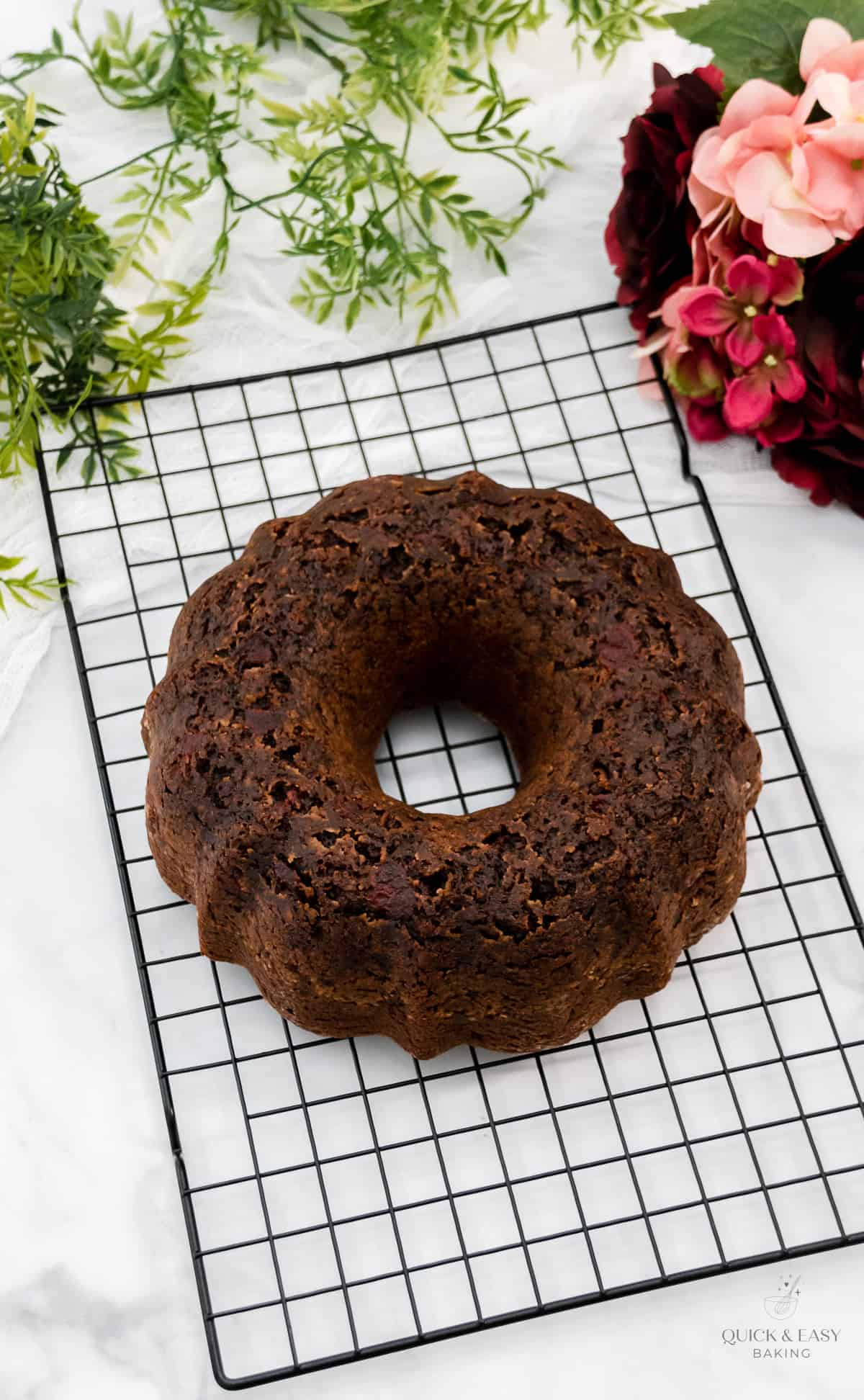 Large bundt cake with cherries cooling on a rack.