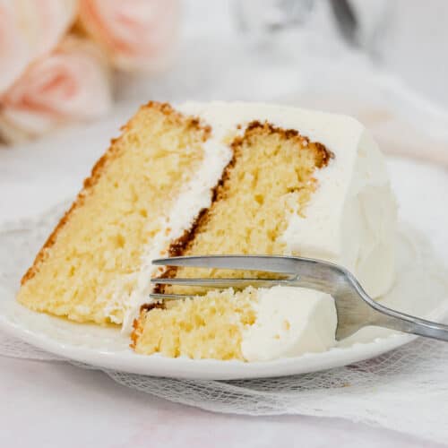 Slice of vanilla layer cake on a white plate with a fork.