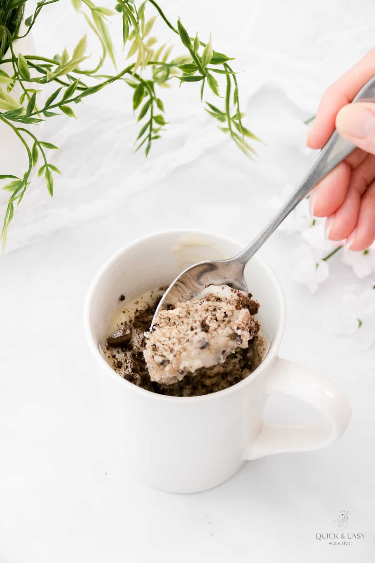 Spoon with a scoop of oreo mug cake in a white mug.