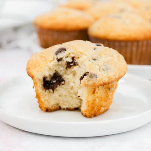 A large bite out of a chocolate chip muffin on a white plate.