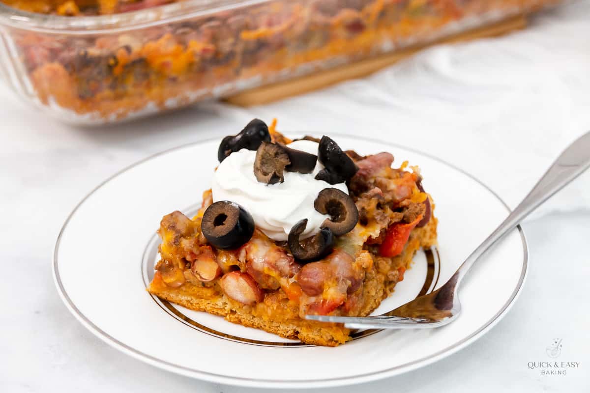 Slice of frito taco pie on a white plate with a fork.