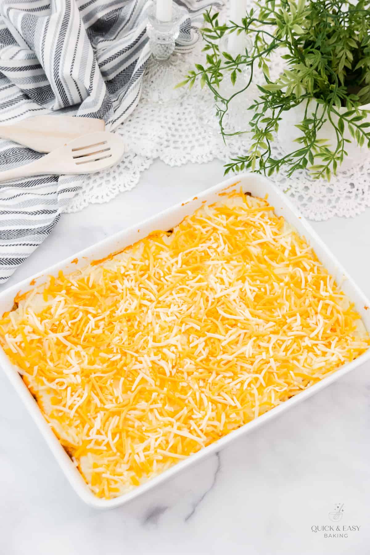 Cheese sprinkled over the top of a cottage meat pie in a white casserole dish.