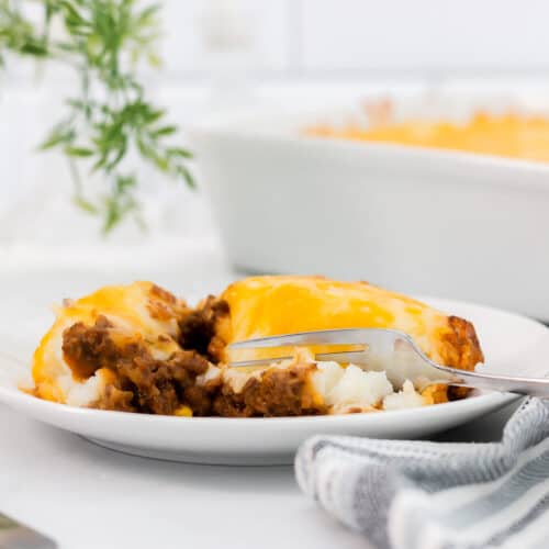 Large helping of shepherds pie with potato topping on a white plate with a fork.