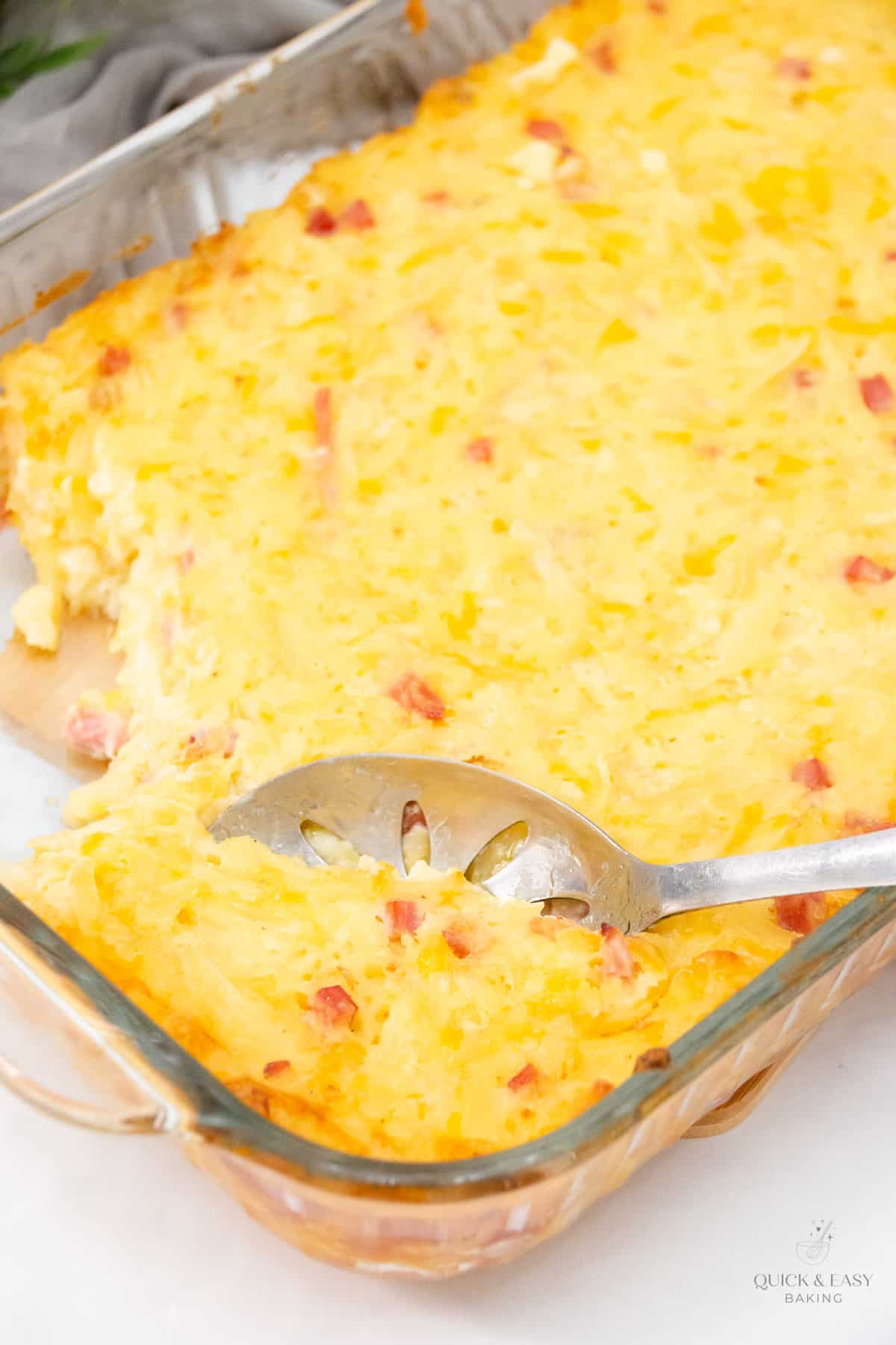 Top view of baked ham cheese and potato casserole with a large sliver spoonl