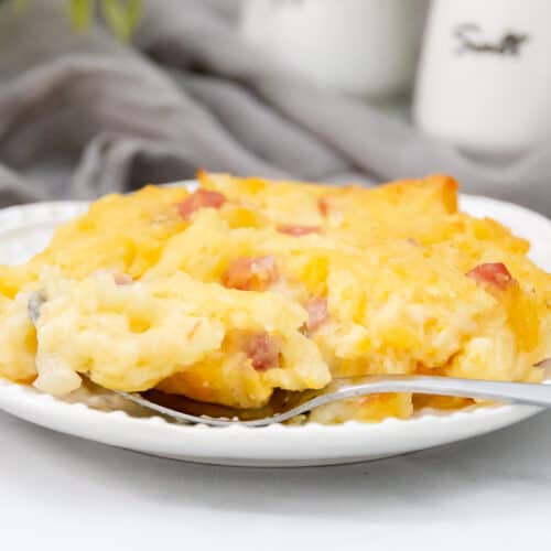 Close up of cheesy ham hashbrown casserole with a fork on a white plate.