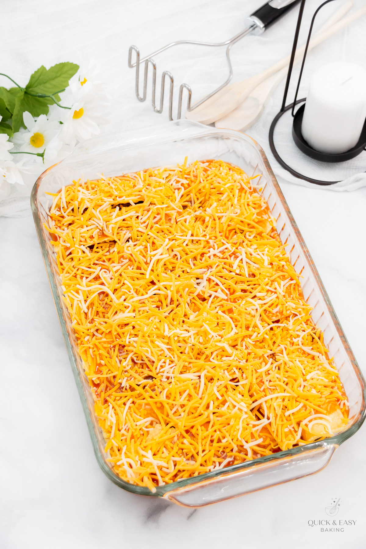 Shredded cheddar cheese covering a baking dish with enchiladas in it.