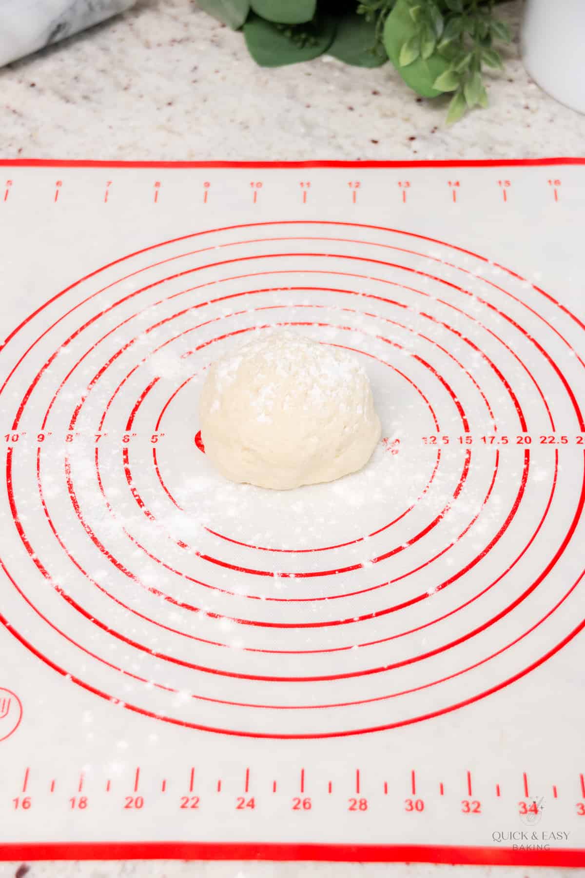 Pizza dough in a ball shape on a nonstick surface.