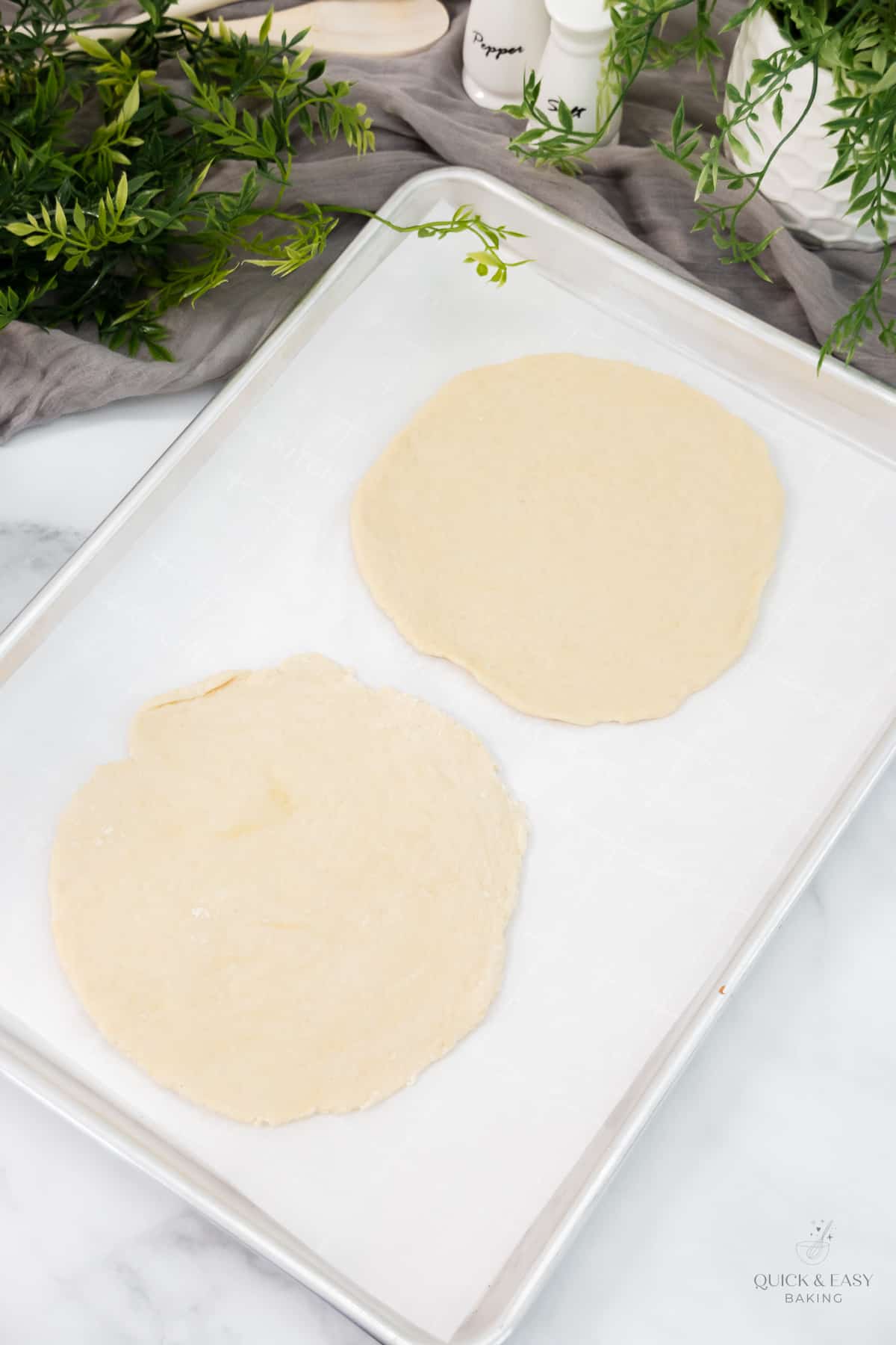 Raw pizza dough in the shape of circles on a baking sheet with parchment paper.