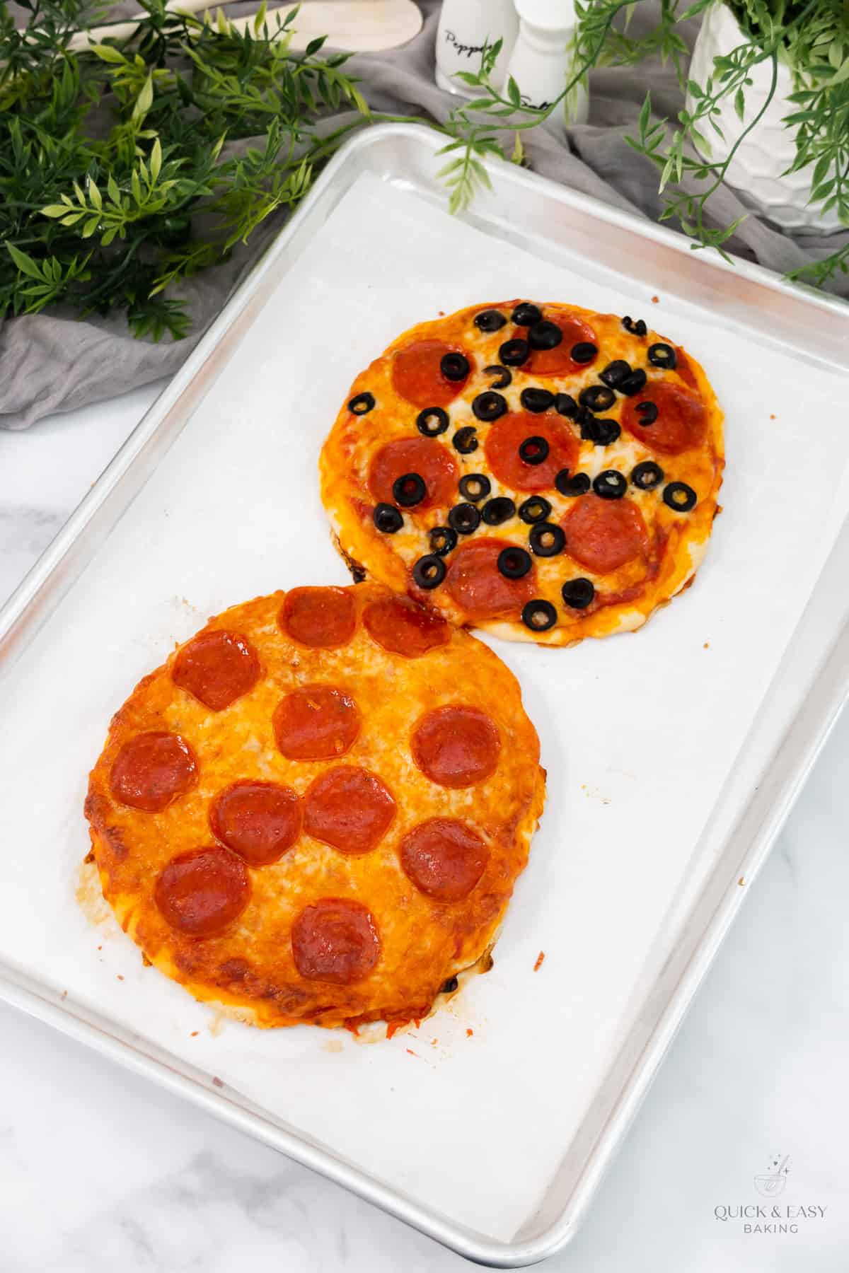 Baked mini personal pizzas on a baking sheet with parchment paper.