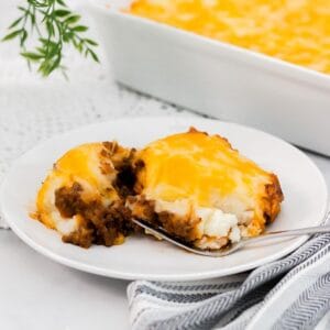 Large slice of cottage pie with mashed potato topping on a plate with a fork.