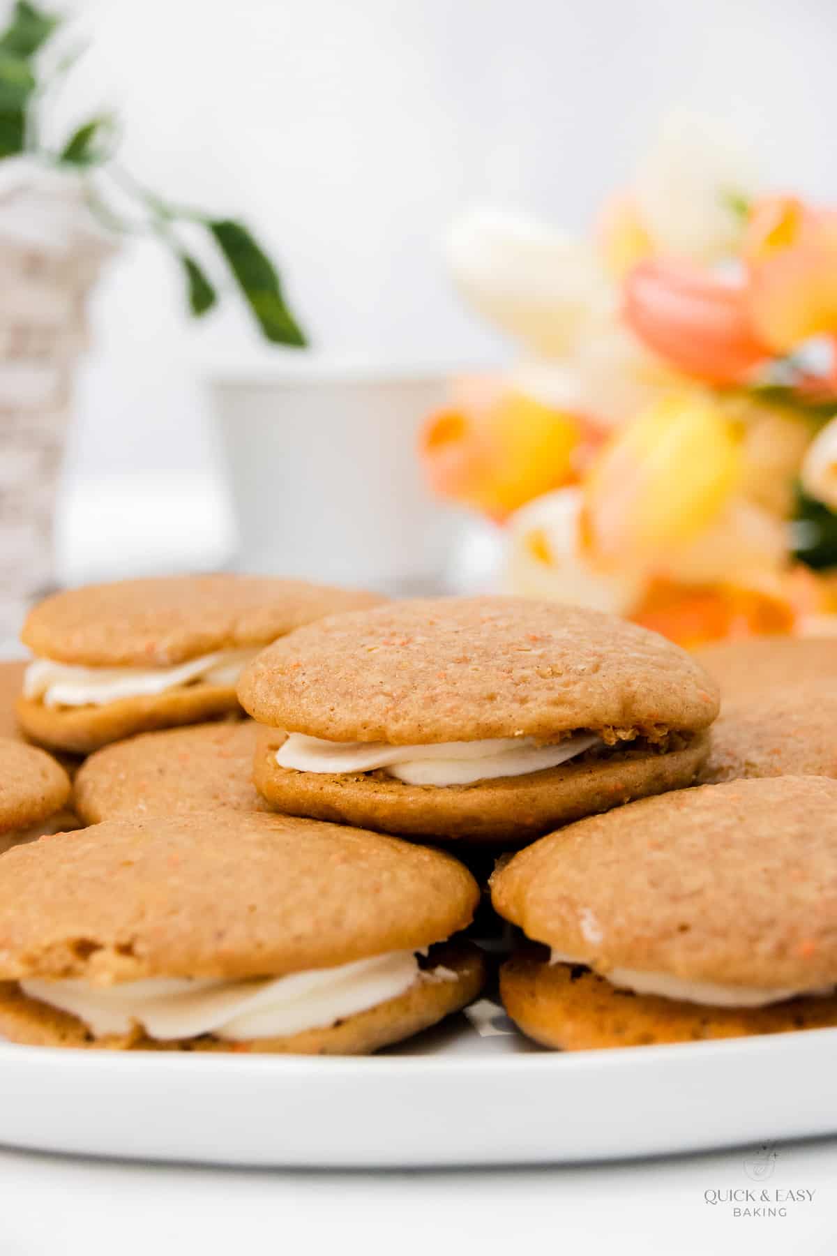 Stacked soft carrot cake cookies with marshmallow filling on a white platter.