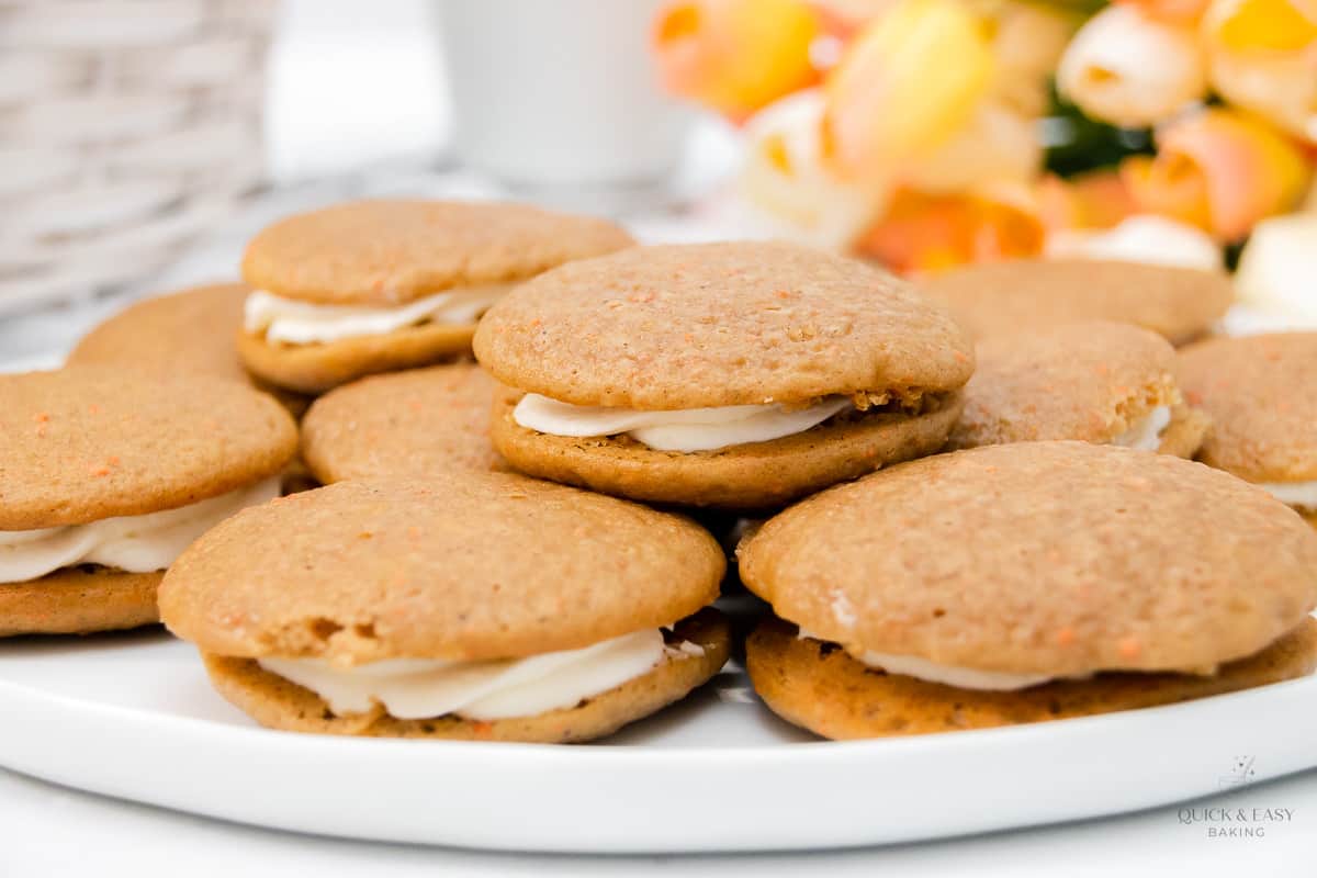 Carrot cake whoopie pies made with marshmallow filling on a white platter.