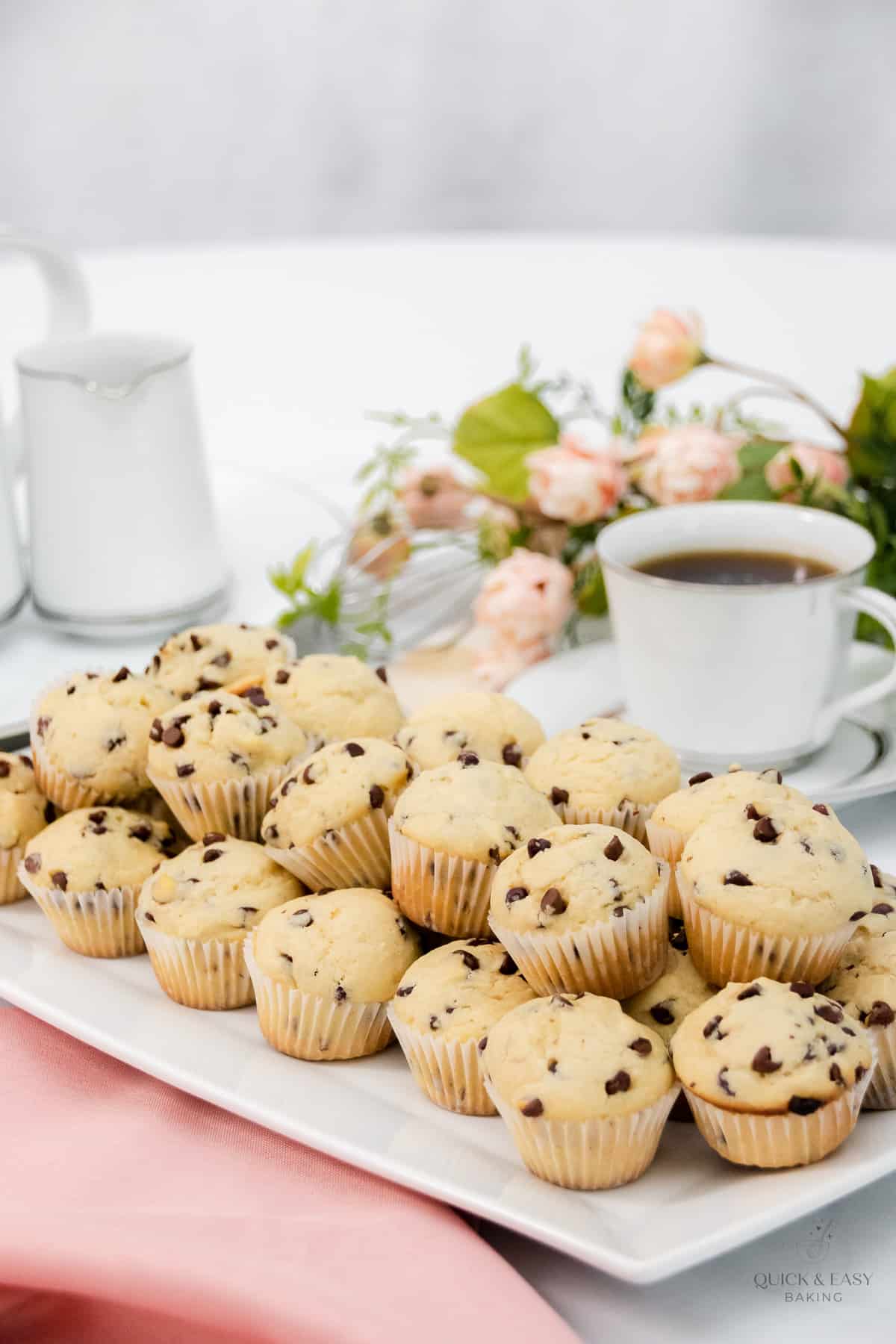 Mini chocolate chip muffins on a white platter with coffee in the background.