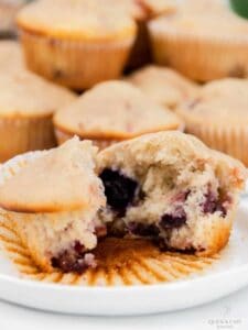 Cut open mixed berry muffin unwrapped on a white plate.