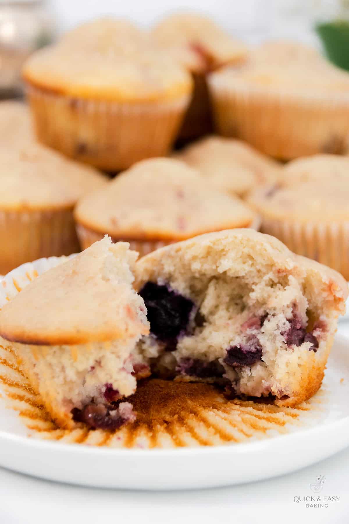 Cut open mixed berry muffin unwrapped on a white plate.