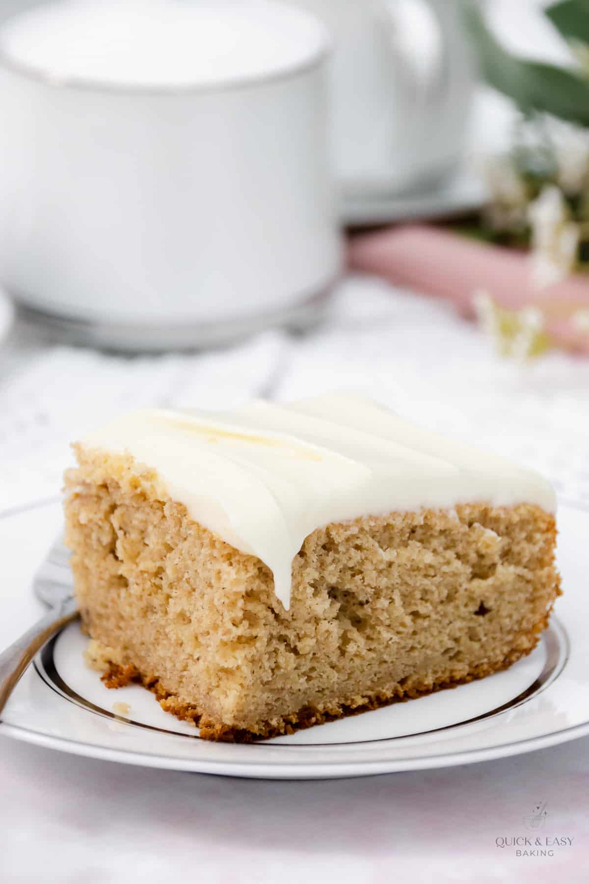 Close up image of banana cake with icing on a white plate and a fork.
