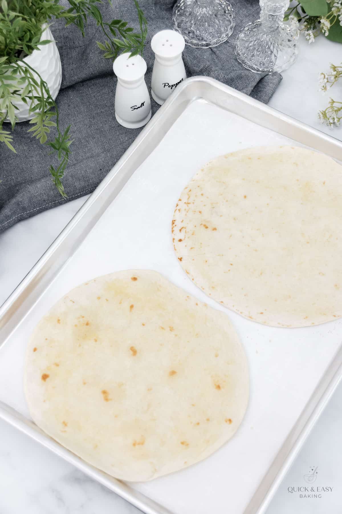 Top down view of flour tortillas with oil on a baking sheet.