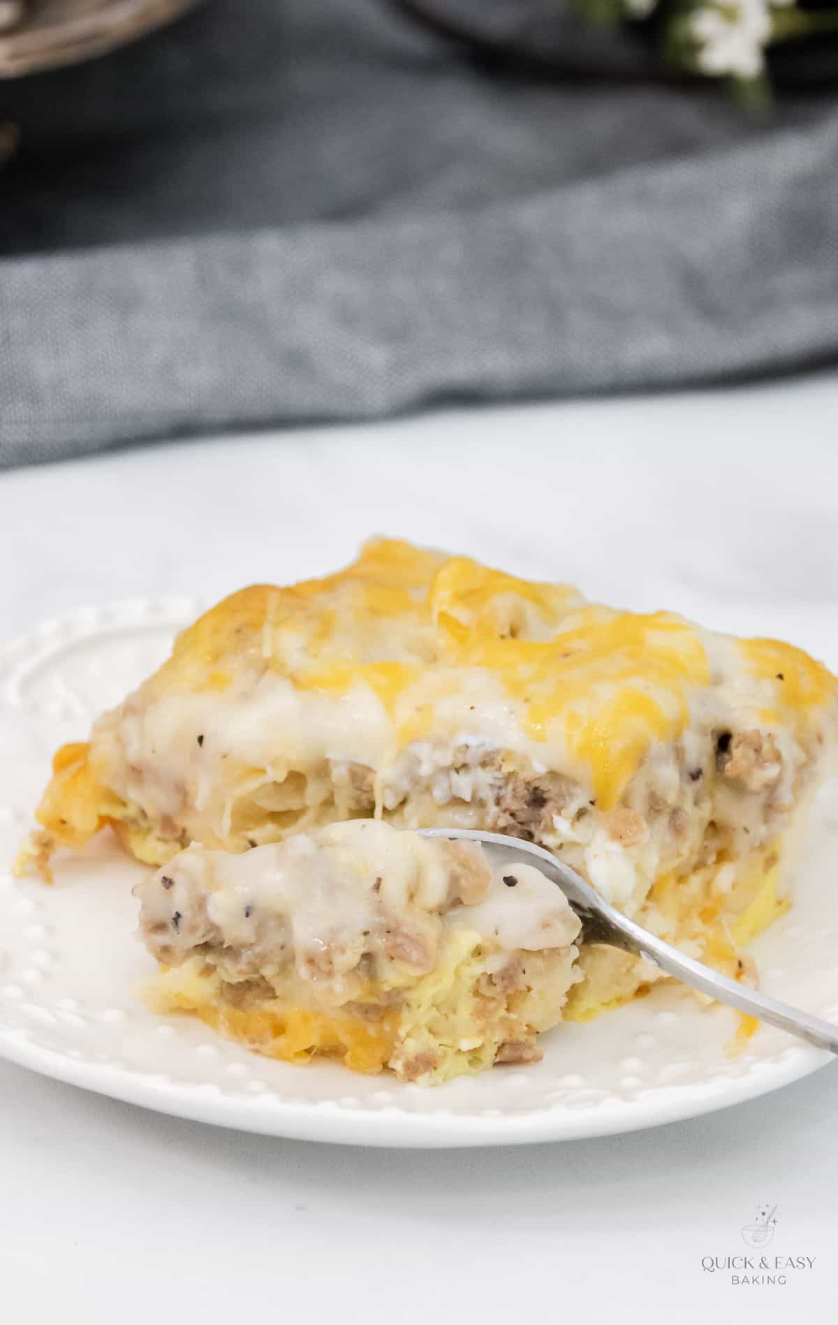Cutting into a gravy and sausage biscuit casserole with a fork on a white plate.