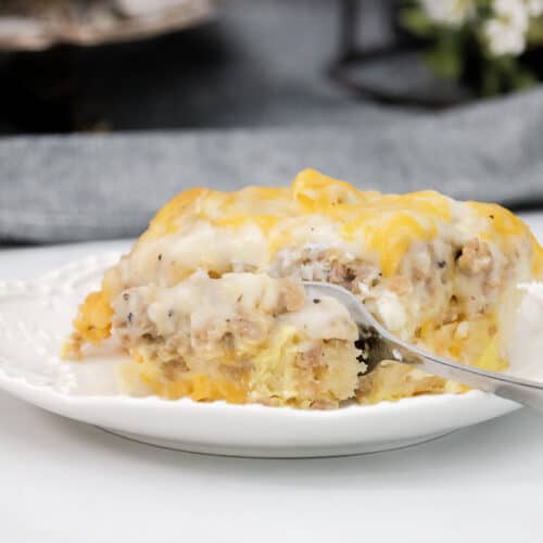 Close up of gravy and sausage biscuit casserole with a fork and a white plate.