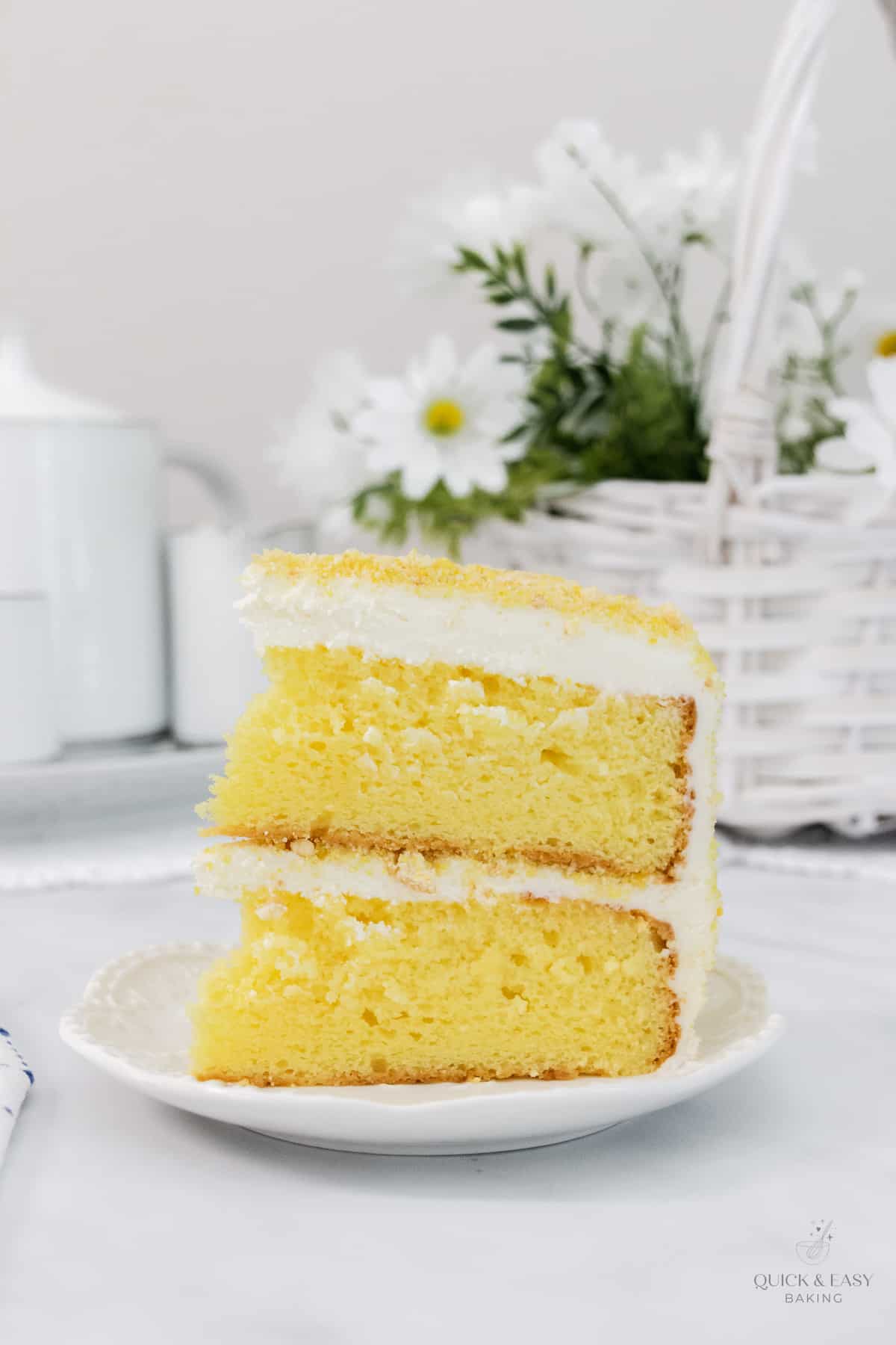 Tall slice of cake with lemon flavor and cream cheese frosting on a white plate.