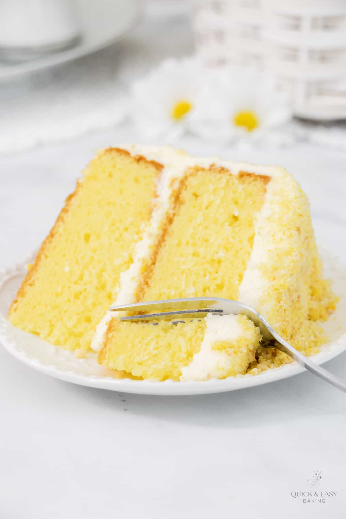 Close up of layer cake that is lemon and buttercream frosting with lemon crunch topping with a fork on a white plate.