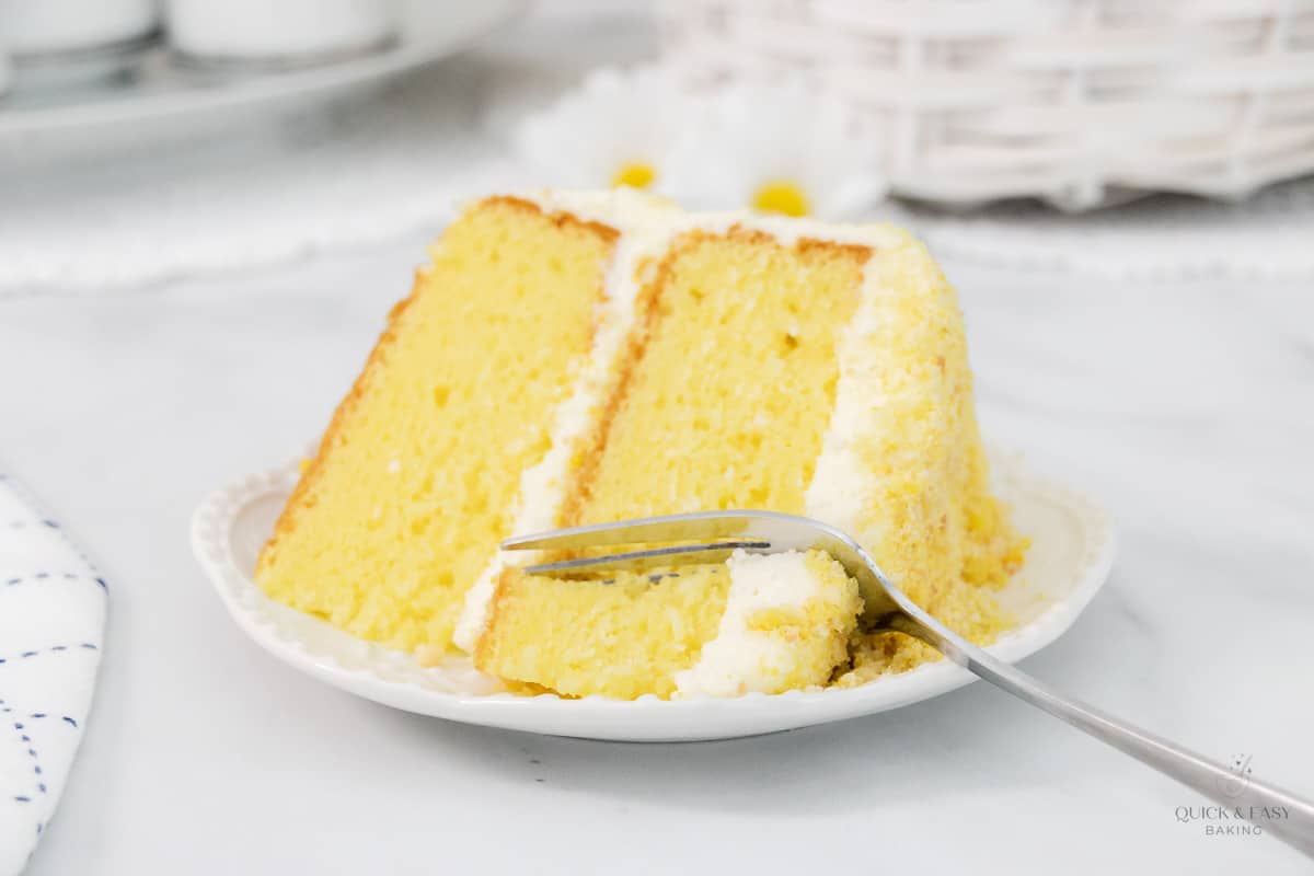 Close up of lemon crunch cake with a fork on a white plate.