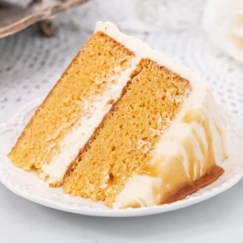 Large slice of caramel cake with frosting on a white plate.