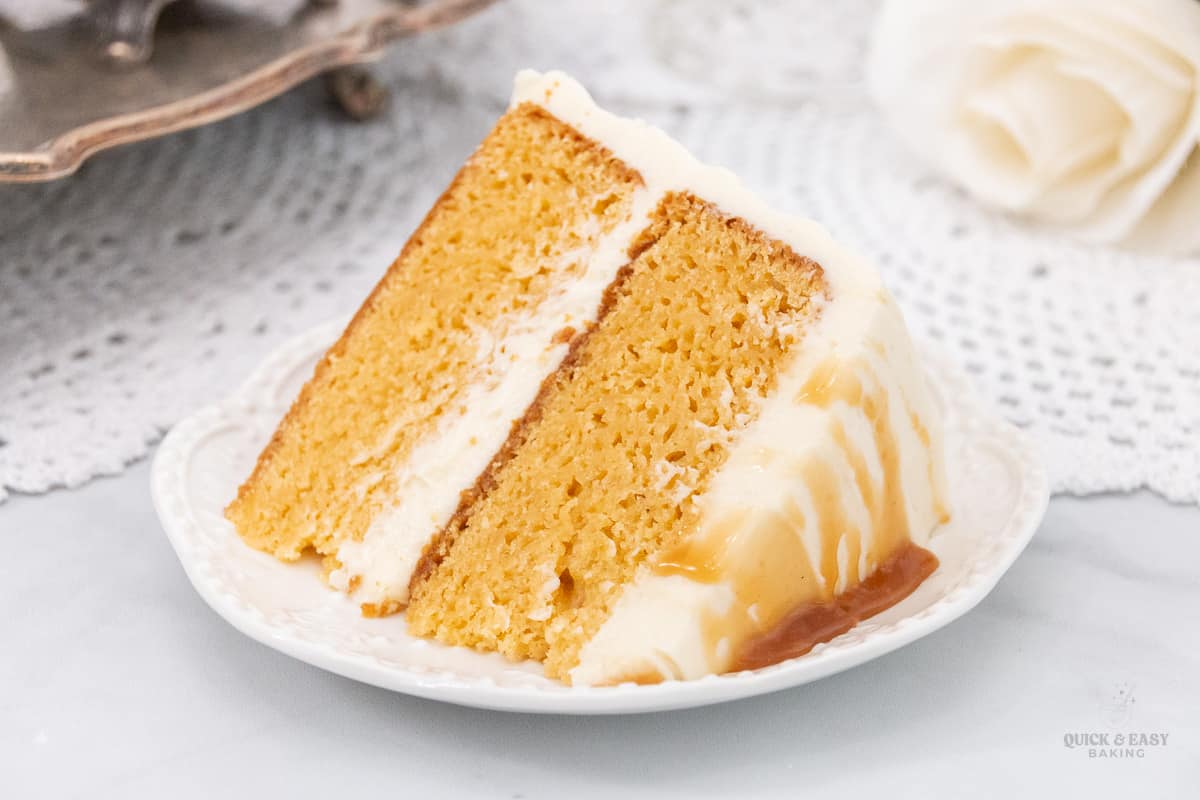 Large slice of caramel cake with frosting on a white plate.